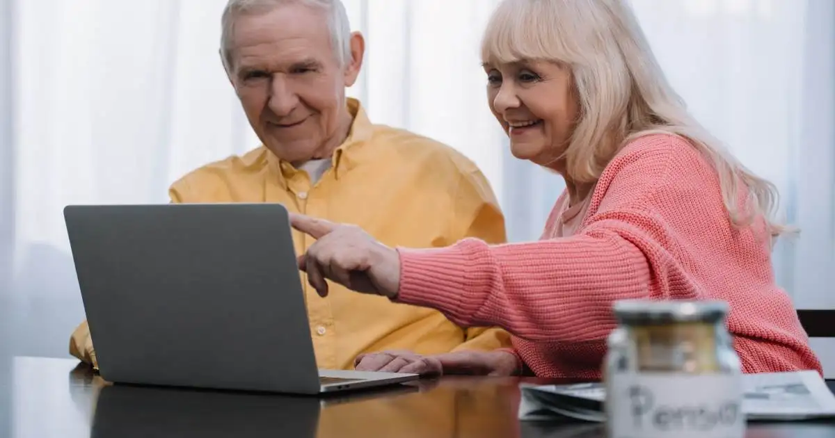 Two elderly individuals smiling while looking at a laptop screen together.